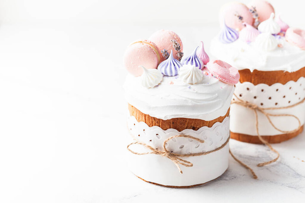 Easter cake, sweet bread decorated with white sugar icing, meringues and macaroons. Kulich wrapped in a craft paper on the white background. - Photo, Image