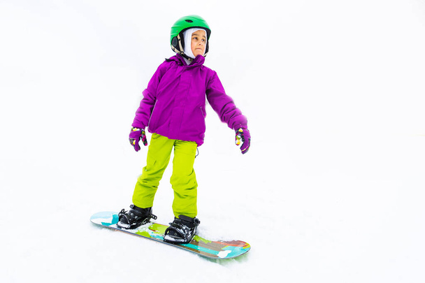 Talviurheilun lumilauta. Pikkutyttö oppii lumilautailemaan lämpimissä talvivaatteissa. Talvitausta. - Valokuva, kuva