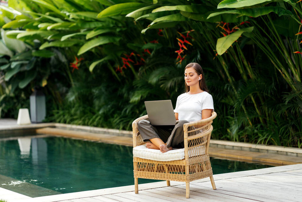 Young woman near swimming pool and working at latop computer - Foto, imagen