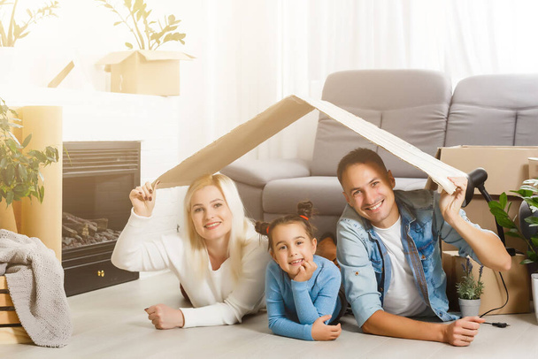 幸せな家族の木製の床に座っている。お父さん、お母さん、お子さんが一緒に楽しんでいます。引越しの家の日、新しい家とデザインのインテリアコンセプト - 写真・画像