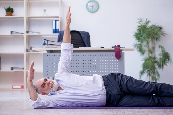 Empleado varón envejecido haciendo ejercicios físicos durante el descanso - Foto, imagen