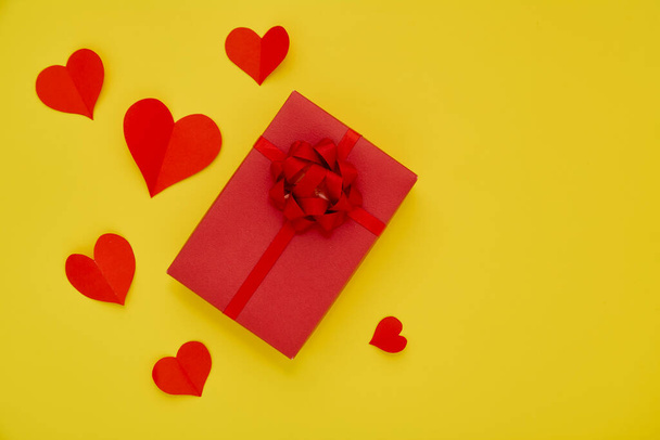 Красная подарочная коробка и бумажные красные сердца на желтом фоне в день влюбленных - Фото, изображение