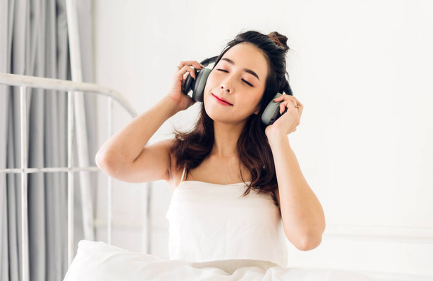 Krásná mladá asijská žena relaxační poslech hudby se sluchátky na posteli doma - Fotografie, Obrázek
