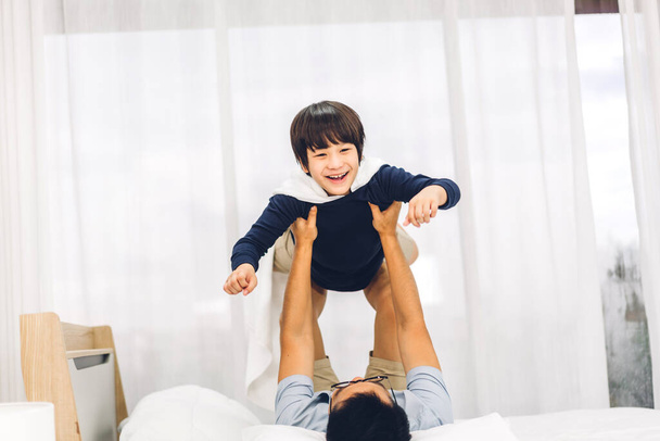 Portrait of enjoy happy love asian family father carrying little asian boy son smiling playing superhero and having fun moments good time on bed at home - Fotografie, Obrázek