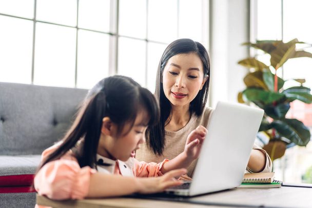 Mère et enfant asiatique petite fille apprendre et regarder ordinateur portable faire des devoirs étudier les connaissances avec l'éducation en ligne e-learning system.children vidéoconférence avec professeur tuteur à la maison - Photo, image