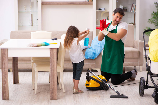 Νεαρός εργολήπτης καθαρίζει το σπίτι με τη μικρή του κόρη. - Φωτογραφία, εικόνα