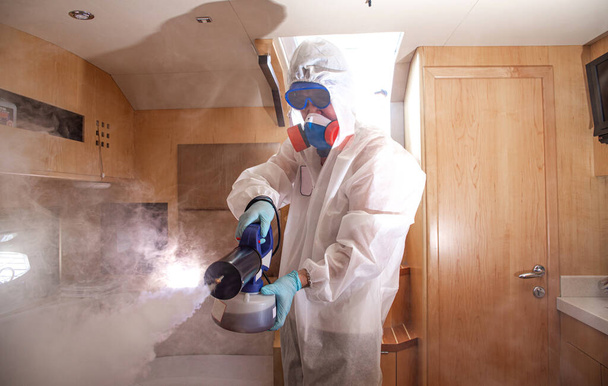 Professioneel in uniform desinfecteert de kamer van covid 19. - Foto, afbeelding