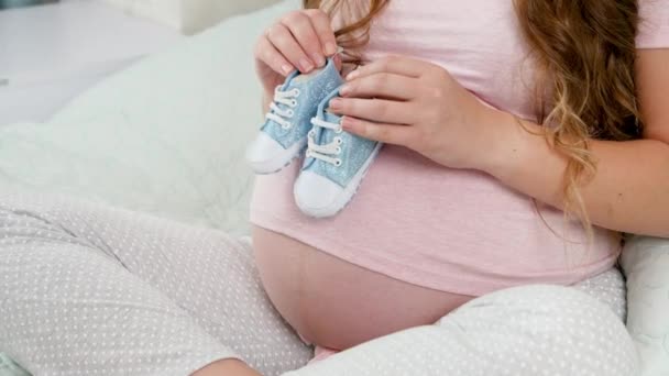 Primer plano de la mujer embarazada joven sosteniendo botas de niño pequeño para bebés y caminando sobre el vientre grande. Concepto de embarazo y embarazo - Metraje, vídeo