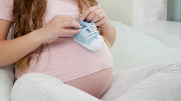 CLoseup de femme enceinte se réveillant sur le gros ventre avec de petites bottes ou des chaussures pour enfants. Concept de grossesse et d'accouchement - Séquence, vidéo