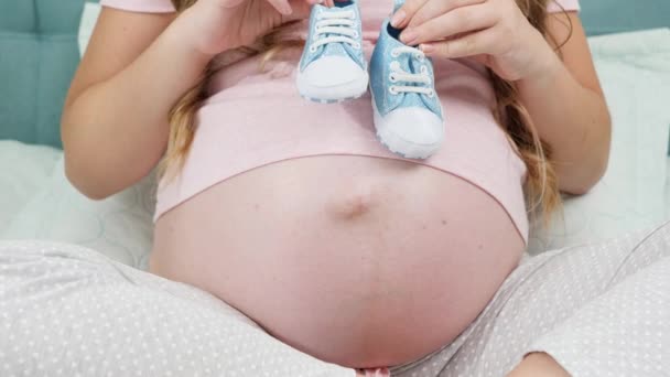 CLoseup de mulher grávida à espera de menino segurando pequenas botas de bebê nas mãos. Conceito de gravidez e esperando bebê - Filmagem, Vídeo