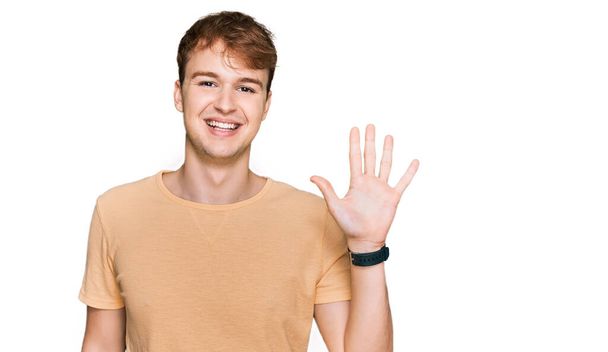 Fiatal kaukázusi férfi alkalmi ruhát visel, mutatva és mutatva az ötös számú ujjaival, miközben magabiztosan és boldogan mosolyog..  - Fotó, kép