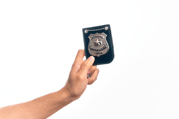 Hand of caucasian young man holding police badge over isolated white background - Photo, Image