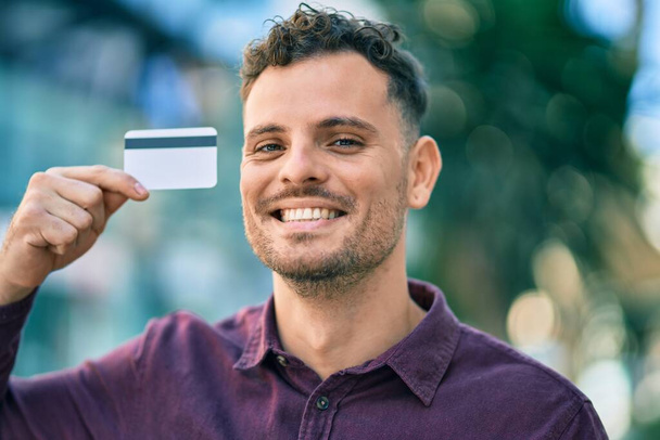 Genç İspanyol adam gülümsüyor, şehirde kredi kartı tutarken mutlu.. - Fotoğraf, Görsel