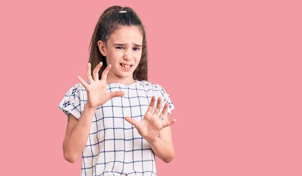 Aranyos spanyol gyerek lány visel alkalmi ruhák undorító kifejezés, elégedetlen és félelmetes csinál undor arc, mert ellenszenv reakció. felemelt kézzel  - Fotó, kép