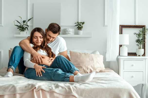 Pregnant girl with her husband lie on the bed. Beautiful belly of a young attractive pregnant girl. Family, marriage, childbirth concept - Photo, image