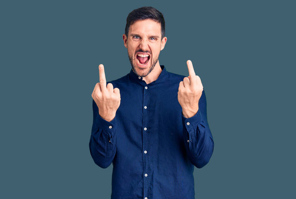 Young handsome man wearing casual shirt showing middle finger doing fuck you bad expression, provocation and rude attitude. screaming excited  - Foto, afbeelding