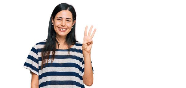 Piękna młoda kobieta w luźnych ubraniach pokazując i wskazując palcami numer trzy uśmiechając się pewny siebie i szczęśliwy.  - Zdjęcie, obraz