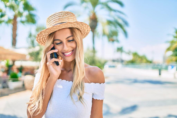 Young blonde tourist girl smiling happy talking on the smartphone at the city. - 写真・画像
