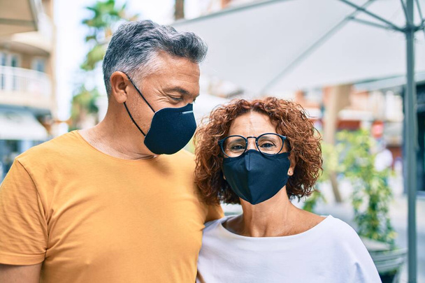 Middelbare leeftijd koppel dragen coronavirus bescherming masker lopen op straat van de stad. - Foto, afbeelding