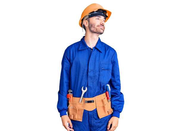 Jovem hispânico vestindo uniforme de trabalhador sorrindo olhando para o lado e olhando para longe pensando.  - Foto, Imagem
