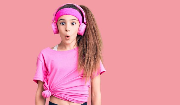 Cute latynoski dziecko dziewczyna noszenie ubrania siłowni i za pomocą słuchawek boi się i wstrząśnięty z zaskoczenia wyraz twarzy, strach i podekscytowany.  - Zdjęcie, obraz