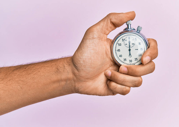 Hand of young hispanic man using stopwatch over isolated pink background. - Foto, imagen