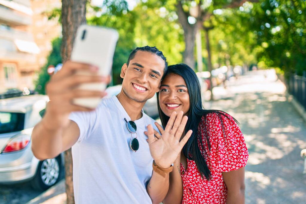 Joven pareja latina sonriendo feliz usando smartphone para videollamada en la calle de la ciudad. - Foto, Imagen