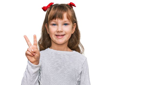 Маленькая белая девочка, одетая в повседневную одежду и показывающая пальцами номер два, улыбаясь уверенно и счастливо.  - Фото, изображение