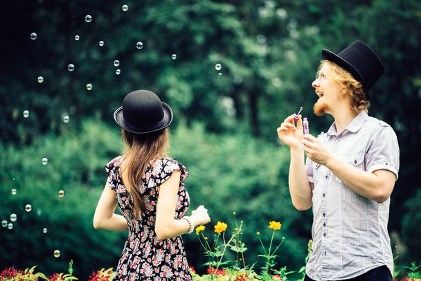 Happy funny hipster couple playing together blowing soap bubbles outdoor in spring park. - Fotoğraf, Görsel