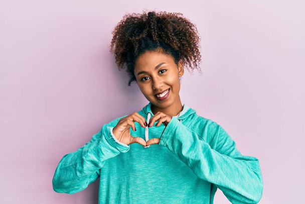 Mulher americana africana bonita com cabelo afro vestindo camisola casual sorrindo no amor mostrando símbolo do coração e forma com as mãos. conceito romântico.  - Foto, Imagem