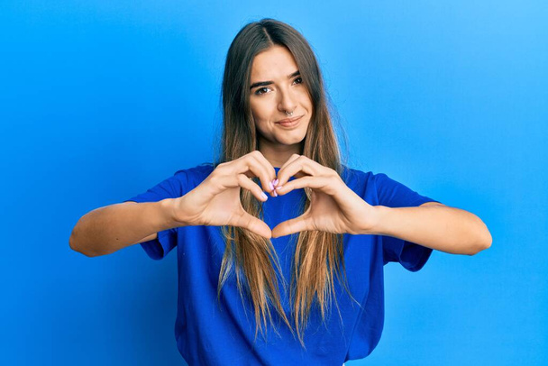 Young hispanic woman wearing casual clothes smiling in love doing heart symbol shape with hands. romantic concept.  - Fotó, kép