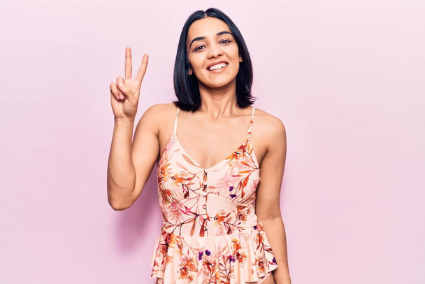 Joven hermosa mujer latina con ropa casual mostrando y señalando hacia arriba con los dedos número dos mientras sonríe confiado y feliz.  - Foto, Imagen