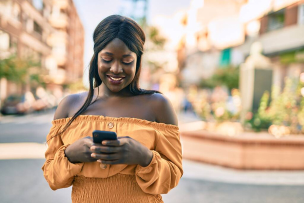 jong Afrikaans amerikaans vrouw glimlachen gelukkig met behulp van smartphone in de stad. - Foto, afbeelding