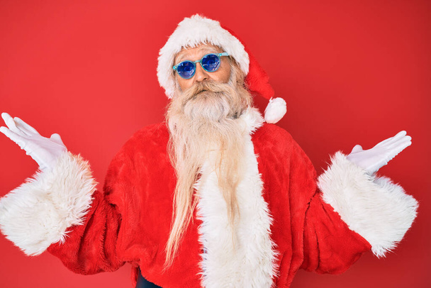 Alter älterer Herr in Weihnachtsmann-Kostüm und Sonnenbrille feiert Sieg mit glücklichem Lächeln und Siegerausdruck mit erhobenen Händen  - Foto, Bild