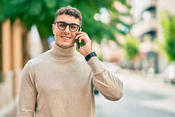 Junger hispanischer Mann mit Brille spricht auf Smartphone in der Stadt. - Foto, Bild