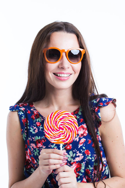 Beautiful smiling woman in summer dress with lollipop in sunglasses isolated on white, background - Fotó, kép