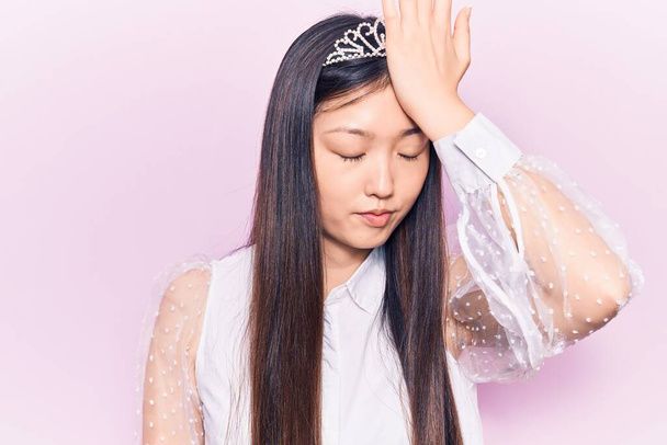 Junge schöne chinesische Frau trägt Prinzessinnenkrone überrascht mit der Hand auf dem Kopf für Fehler, erinnern Sie sich an Fehler. Vergessenes, schlechtes Gedächtnis.  - Foto, Bild