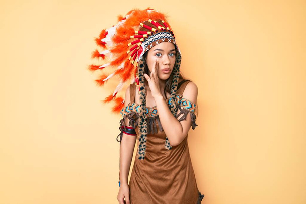 Young beautiful latin girl wearing indian costume hand on mouth telling secret rumor, whispering malicious talk conversation  - Photo, Image