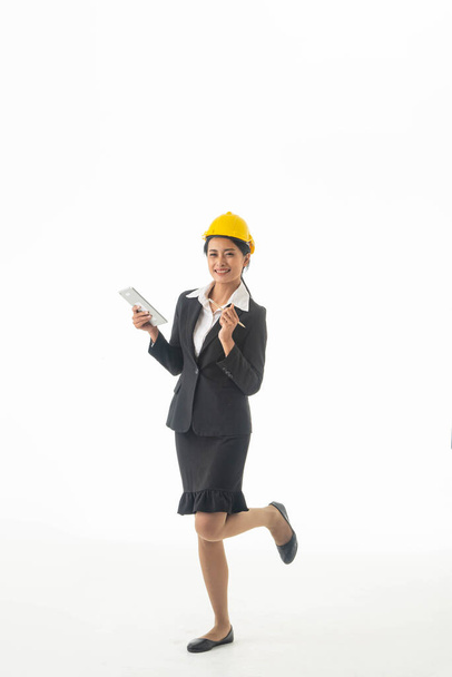 Junge Ingenieurin trägt schwarzen Anzug und gelben Schutzhelm mit Zettel oder Tablet auf weißem Hintergrund. - Foto, Bild