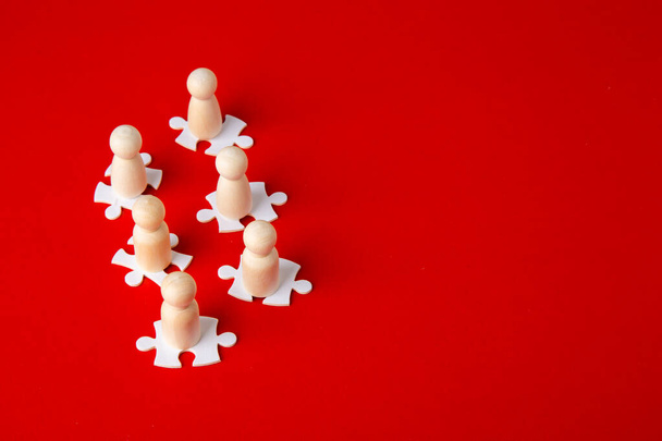 Wooden figures on puzzles on red background as a symbol of team building. Organization group people in business. Cooperation and partnership. - Photo, Image