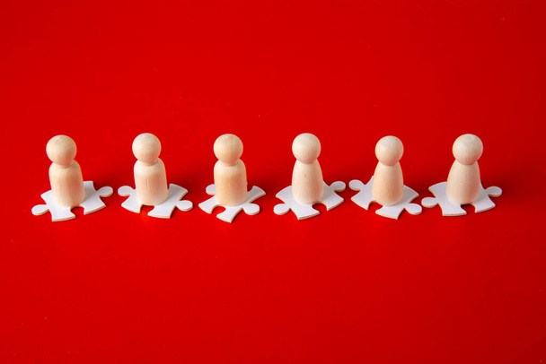 Holzfiguren auf Puzzles auf rotem Hintergrund als Symbol der Teambildung. Organisationsgruppe Menschen in der Wirtschaft. Zusammenarbeit und Partnerschaft. - Foto, Bild