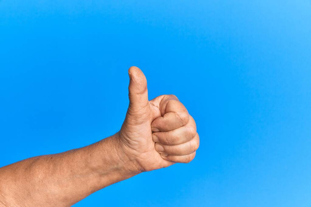 Hand van senior Spaanse man over blauwe geïsoleerde achtergrond doet succesvolle goedkeuring gebaar met duimen omhoog, validatie en positief symbool  - Foto, afbeelding