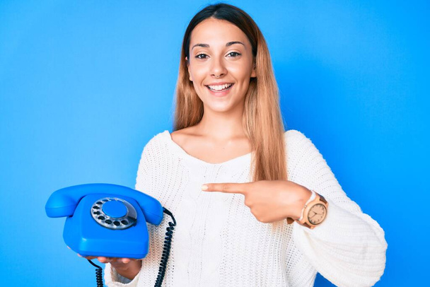 Giovane donna bruna utilizzando telefono vintage sorridente felice indicando con mano e dito  - Foto, immagini