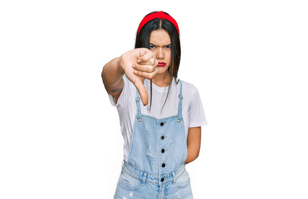 Jong Latijns-Amerikaans meisje draagt nonchalante kleren die er ongelukkig en boos uitzien en afwijzing tonen en negatief met duimen naar beneden gebaar. slechte uitdrukking.  - Foto, afbeelding