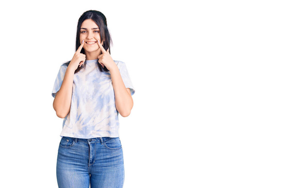 Young beautiful girl wearing casual t shirt smiling with open mouth, fingers pointing and forcing cheerful smile  - 写真・画像