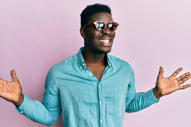 Handsome business black man wearing stylish sunglasses celebrating victory with happy smile and winner expression with raised hands  - Φωτογραφία, εικόνα