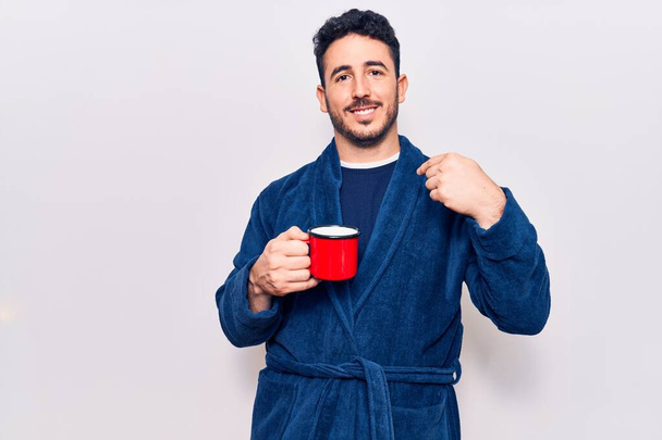 Молодий іспаномовний чоловік у халаті тримає каву вказуючи пальцем до одного себе посміхаючись щасливим і гордим
  - Фото, зображення