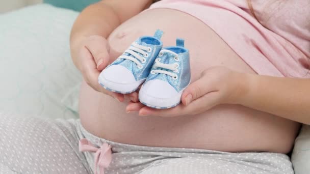 Detailní záběr na oslavu miminka. Těhotná žena čeká na chlapečka drží modré novorozené boty na rukou - Záběry, video
