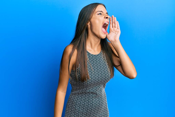 Mujer hispana joven con ropa casual gritando y gritando fuerte a un lado con la mano en la boca. concepto de comunicación.  - Foto, Imagen