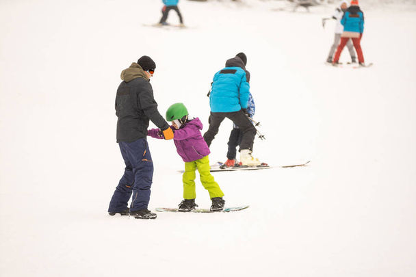 Instruktoren bringen einem Kind auf einem Schneehang das Snowboard bei - Foto, Bild